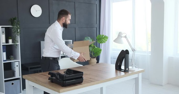 Businessman unpacking carton box and arranging his belongings on new office desk