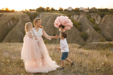 Stylish young boy gives a big flower to his mom in a field at sunset