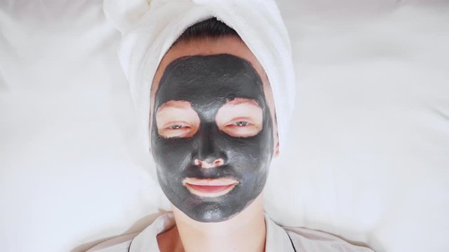 close up face woman with a white towel on her head and black cosmetic mask wellness, spa, skin care