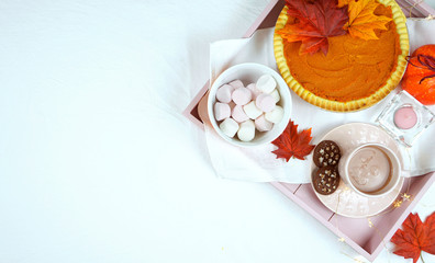 Cozy autumn Thanksgiving in bed flatlay overhead with tray of pumpkin pie and hot chocolate with marshmallows, copy space.