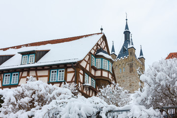 The medieval half-timbered house and the Blue Tower are the sights of the old town of Bad Wimpfen, Germany. The tiled roof of the house, trees and shrubs are densely covered with snow. Winter photo
