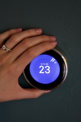 Female Hand changes temperature of smart home thermostat on blue wall in celsius.