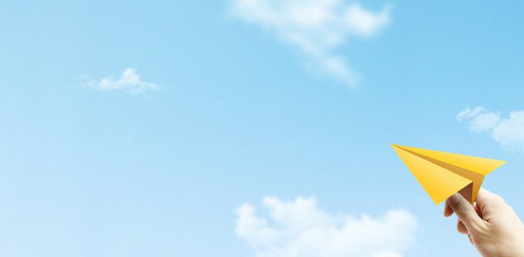 Freedom Concept : Hand holding yellow paper plane and throwing to blue sky.
