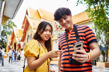 young thai couple looking at smartphone in front of Wat Phrathat Doi Suthep temple in chiang mai thailand
