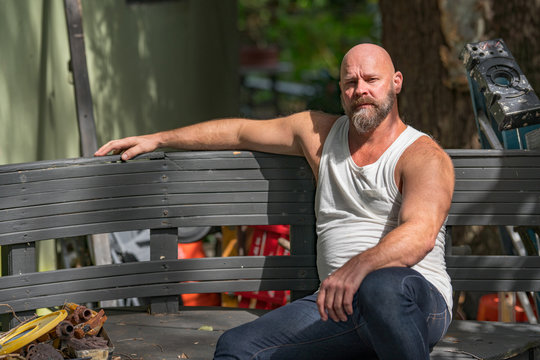 Photo Of A Mature Man Sitting On A Bench Wearing A Tank Top And Blue Jeans