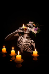 Woman in ghost bodypaint holding candle light in to her mouth on dark background