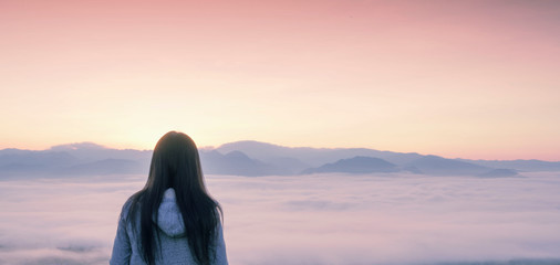 Long hair woman wearing jacket with hood standing on the top of the mountain look over sky with...