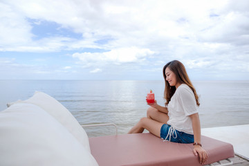 A beautiful asian woman drinking watermelon juice while sitting by the sea