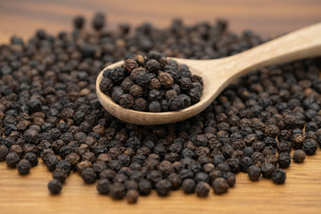 Dry heap black pepper isolated on wooden chopper board with wooden spoon