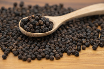 Dry heap black pepper isolated on wooden chopper board with wooden spoon