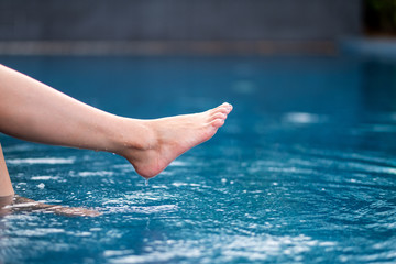 Closeup image of legs and barefoot kicking and soaking water in the pool