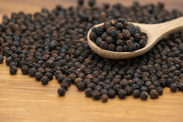 Dry heap black pepper isolated on wooden chopper board with wooden spoon