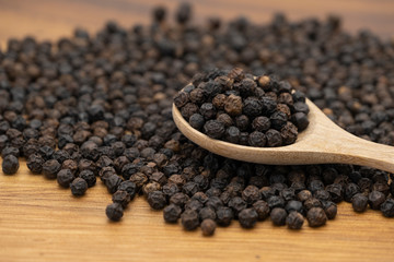 Dry heap black pepper isolated on wooden chopper board with wooden spoon