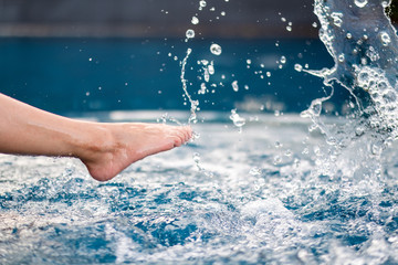 Closeup image of legs and barefoot kicking and splashing water in the pool