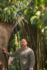 Naklejka na ściany i meble Image of a man posing by a tree in an outdoor garden scene