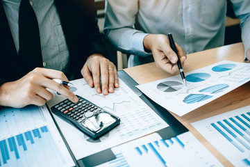 Manager calculates about the company finances by pressing on the calculator on the table with the employee explaining the summary report of the company cost at the office.