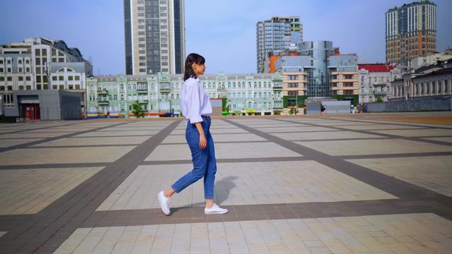 cheerful woman going to the camera female in casual white shirt and sneakers architecture and cityscape background