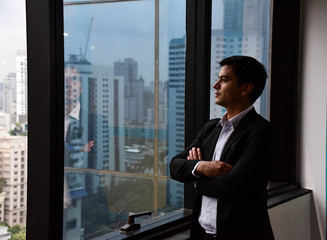 Fototapeta premium A handsome businessman look out of his office window on the tall building and think about the company development and new project in the future/Vision/Business going forward