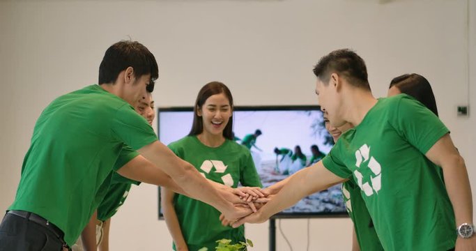 4K Volunteer Team having a meeting. Group of young asian people volunteers in green t-shirts stack hands together as unity and teamwork in modern office.