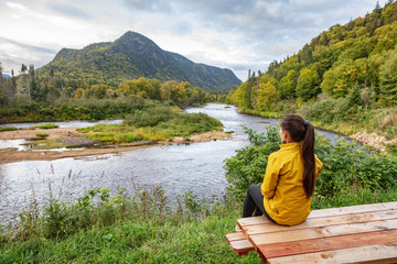 Camping nature woman sitting at picnic table enjoying view of wilderness river in Quebec and autumn foliage forest, Canada travel. Parc de la Jacques-Cartier, Quebec.