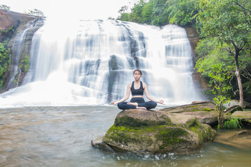Young asain women practicing yoga at front of grand waterfall.