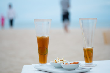 Glass of cold iced tea with sliced lemons on the beach with seascape background