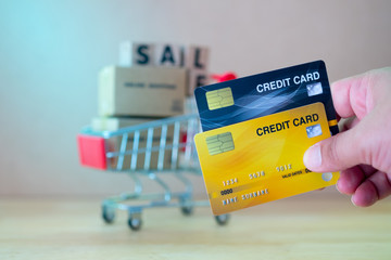 Holding credit card to payment with small red shopping cart background.