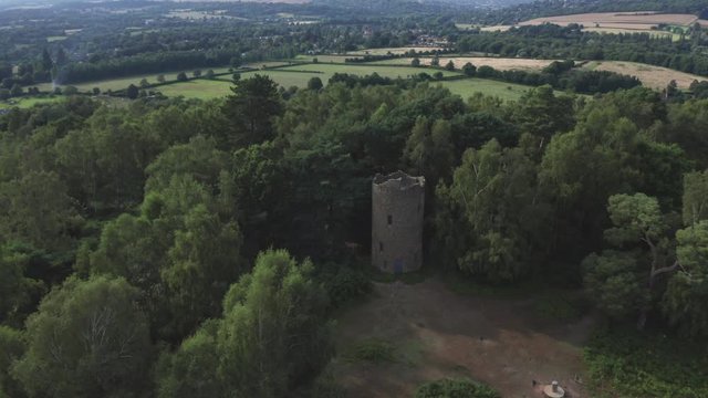 Aerial shot of a folly tower in the English countryside.
Shot rising up high.