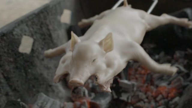 A slow-motion, closeup shot of a split duck carcass in an iron skewer placed over the burning charcoal fire in an open rotisserie beside the road.