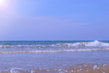 Sandy sea shore in bright sunny day with sparkling waves lapping on the beach and form a white foam. Waves rolling in tubes. Beautiful blue seascape and nature background.