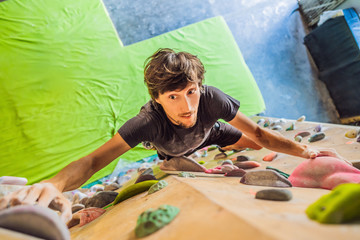 Muscular man practicing rock-climbing on a rock wall indoors