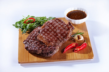 juicy delicious medium fried meat steak on a wooden cutting board, with pepper, garlic, herbs and tomato sauce. Steak for a restaurant on a white background