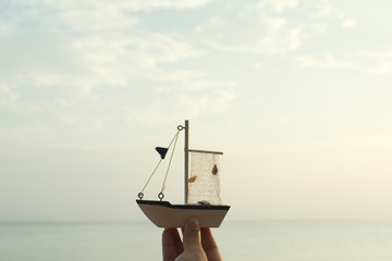 Hand holding model boat and the sea background.