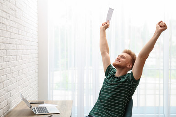 Happy young lottery winner with ticket at table