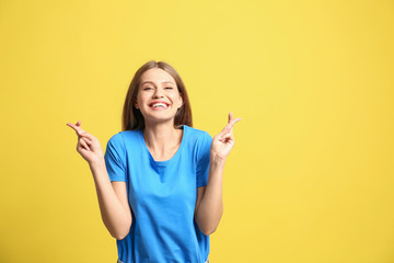 Portrait of hopeful woman with crossed fingers on yellow background