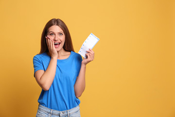 Portrait of excited young woman with lottery ticket on yellow background, space for text - obrazy, fototapety, plakaty