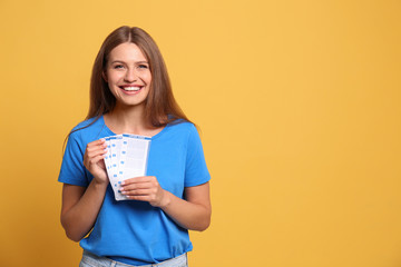 Portrait of happy young woman with lottery tickets on yellow background, space for text
