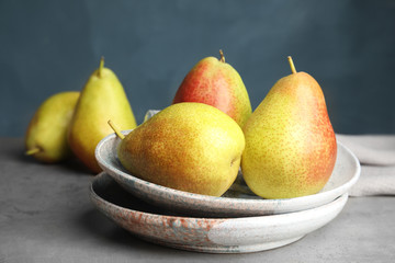 Plates with ripe juicy pears on grey stone table against blue background