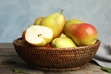Wicker basket with ripe juicy pears on brown wooden table against blue background