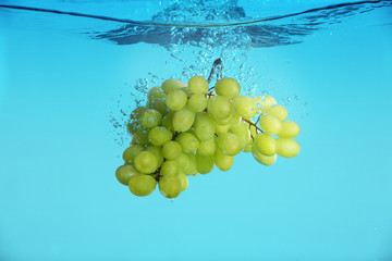 Fresh ripe grapes falling in water on grey background