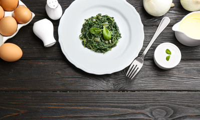 Flat lay composition with cooked spinach on black wooden table. Healthy food