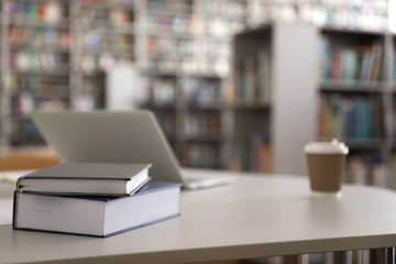 Books, laptop and drink on table in library