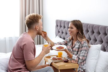 Happy young couple having romantic breakfast on bed at home