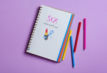 Notebook with phrase "SEX EDUCATION" on violet background, flat lay
