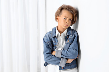 Cute little boy in casual outfit near white wall in room. Space for text