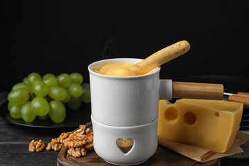 Pot of tasty cheese fondue and bread stick on black wooden table