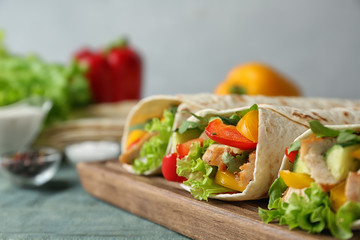 Board with delicious meat tortilla wraps on blue wooden table against grey background, closeup