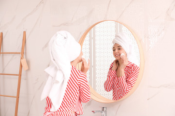 Young woman with towel on head near mirror in bathroom