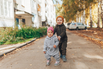Cute 1 year old baby girl and 3 years old boy walking outdoors wearing in stylish overalls