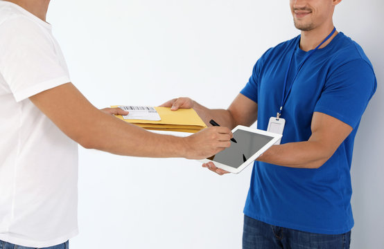 Young courier with envelopes and client signing on tablet against white background, closeup - Powered by Adobe